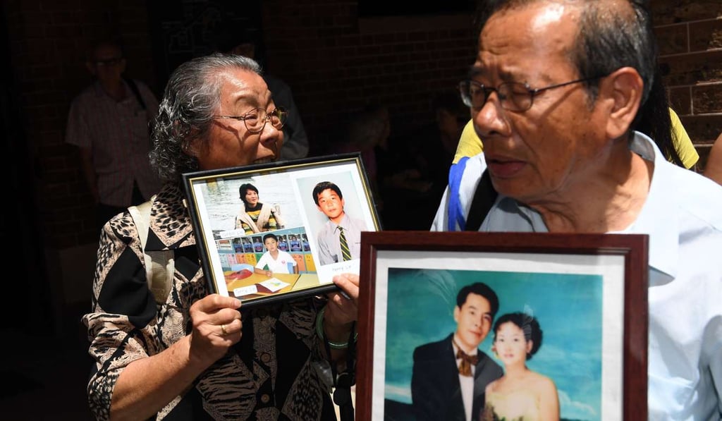Feng Qing Zhu (left) and Yang Fei Lin hold family portraits of their murdered son Norman Min Lin and his family as they leave the New South Wales Supreme Court in Sydney on Monday. Their daughter’s husband, Robert Xie, carried out the killings. Photo: EPA