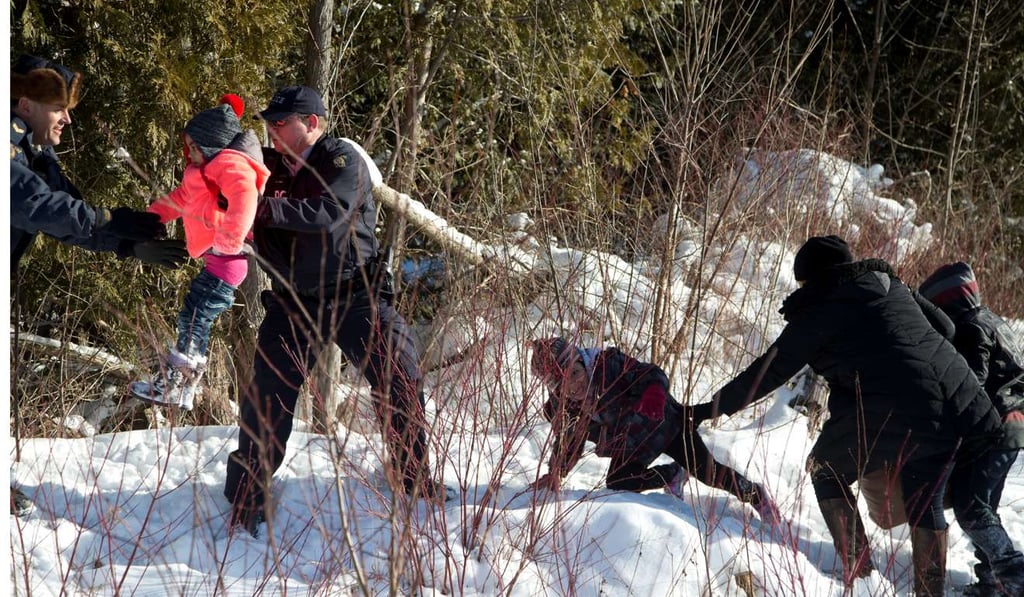 Royal Canadian Mounted Police officers assist a child from a family that claimed to be from Sudan as they walk across the US-Canada border into Hemmingford, Canada, on February 17. Photo: Reuters