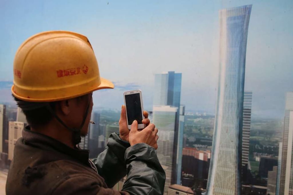 A Chinese construction worker uses his mobile to take a photo of a poster placed outside of a construction site showing the design of future high-raise buildings and skyscrapers in Beijing.