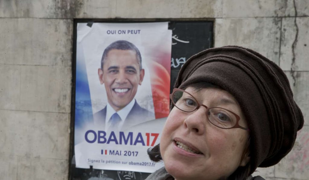 American Sarah Wachter stands next to a campaign poster with the picture of former U.S. President Barack Obama reading in French