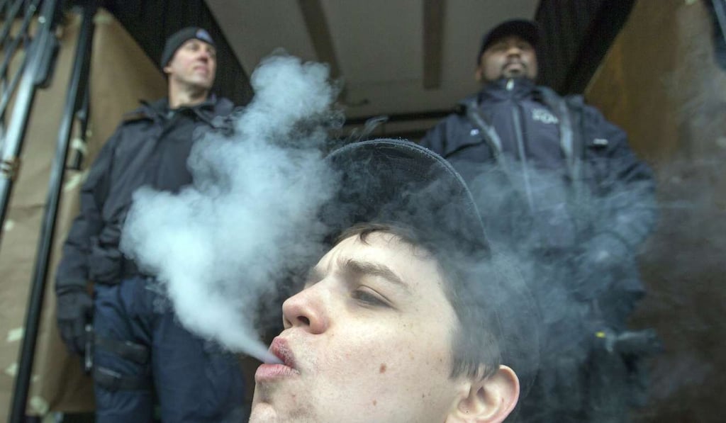 A young man smokes a joint as police officers stand outside a Cannabis Culture shop during a police raid in Vancouver, British Columbia, on Thursday. Photo: AP