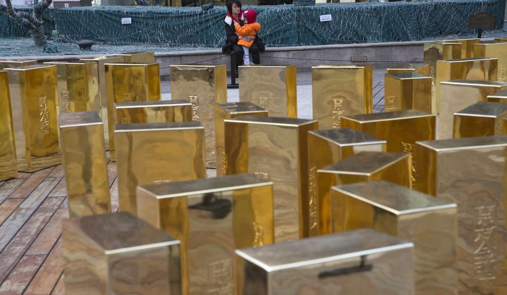 A woman comforts a child near replicas of gold bars at a mall in Beijing, China. Gold prices weakened further on expectations of US rate rise next week. Photo: AP