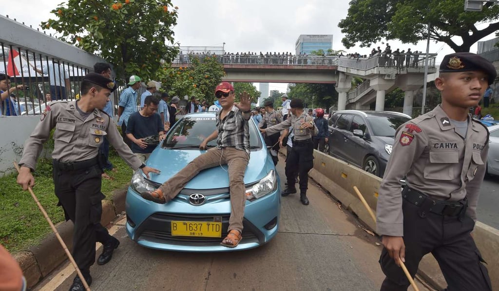 Police escort a taxi taking part in a rally against drivers working for ride-hailing services in Jakarta. Photo: AFP