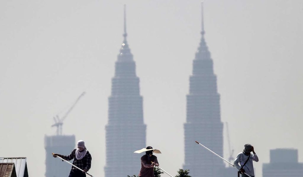 Construction workers paint a factory roof against the Twin Towers of Kuala Lumpur, Malaysia. Photo: EPA Construction workers paint a factory roof against the Twin Towers of Kuala Lumpur, Malaysia. Photo: EPA