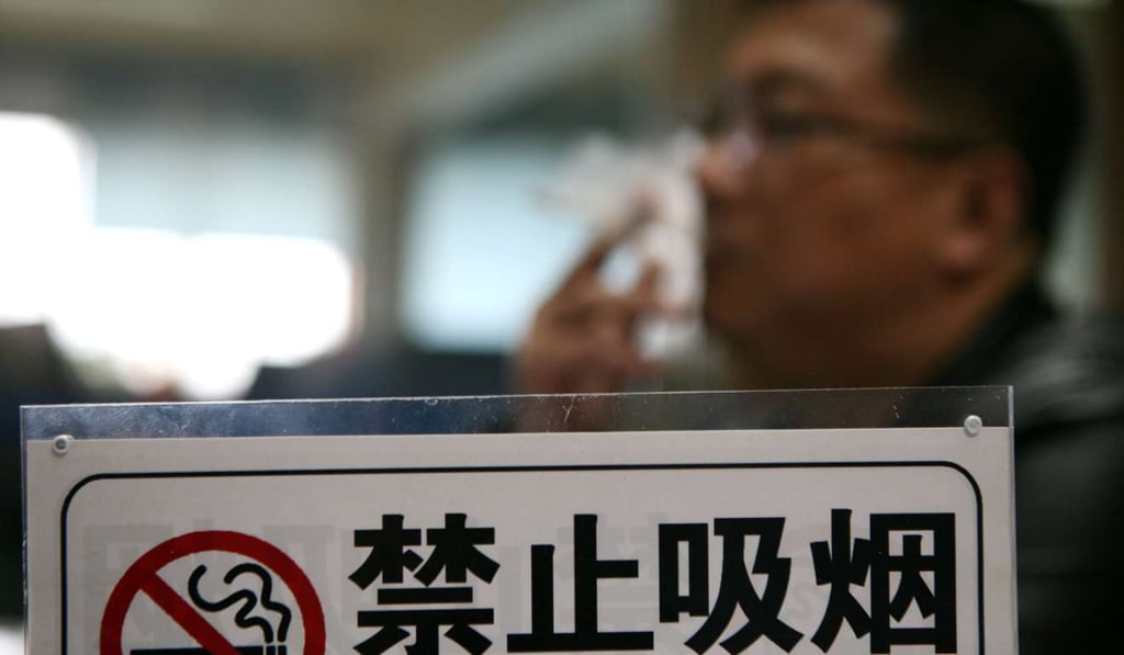 A man smokes behind a no-smoking sign in Huaian in Jiangsu province. Photo: Imaginechina