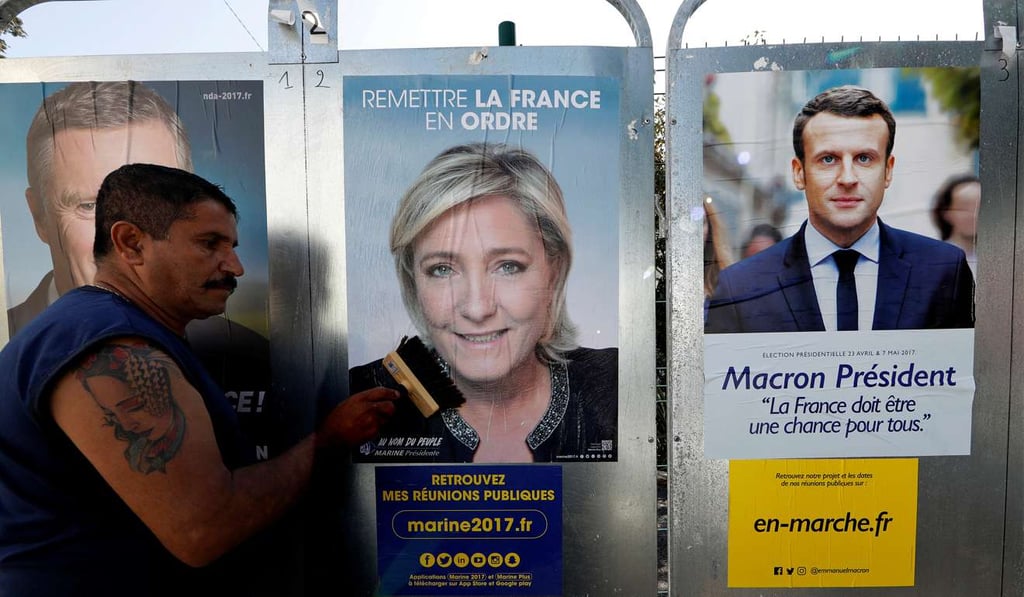 A member of the French National Front (FN) political party pastes a poster for leader Marine Le Pen next to the poster of Emmanuel Macron, head of the political movement En Marche! in Antibes, France. Photo: Reuters