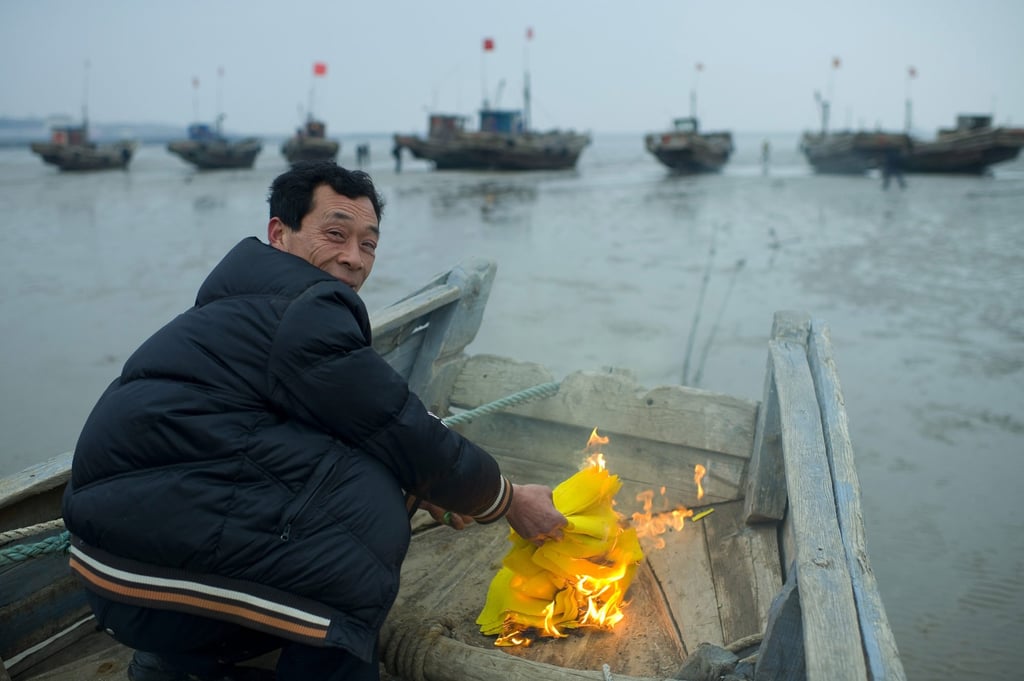 A Chinese fisherman burns joss papers to sacrifice on his fishing boat during the ceremony of sacrifice to the sea God in Zhougezhuang village. Photo: Getty