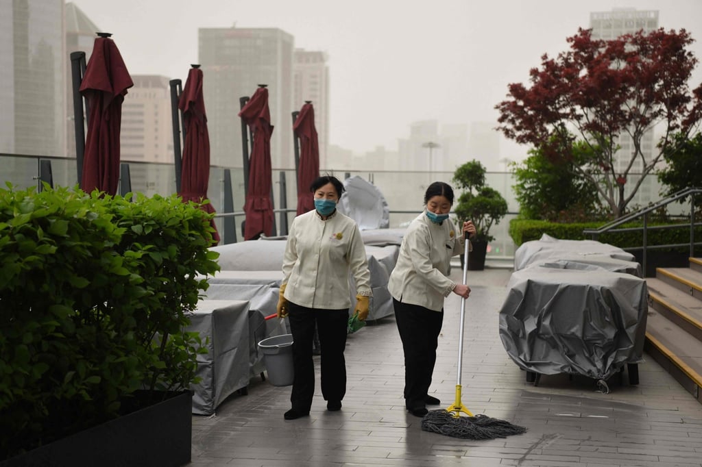 Two workers sweep the floor of an outdoor restaurant in the central business district during a sandstorm in Beijing on Thursday. Photo: AFP
