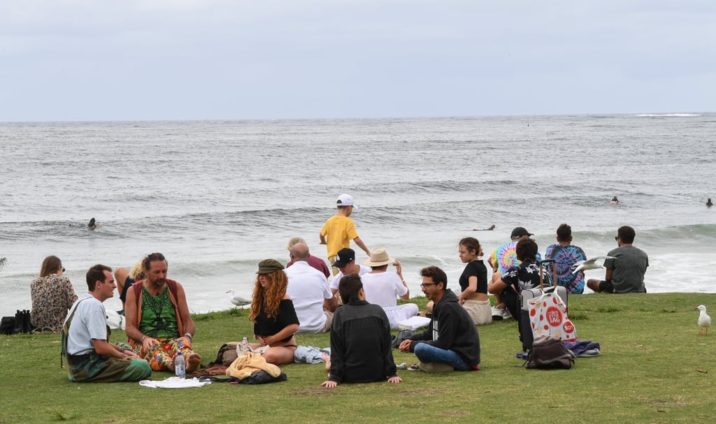 People sit on the grass beside main beach in Byron Bay, Australia. The town receives 2.5 million visitors a year. Photo: Getty Images