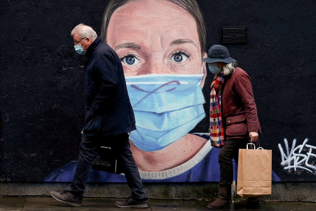 People wearing face masks walk past a mural of a nurse in the centre of Manchester, England, in November 2021. Photo: Reuters