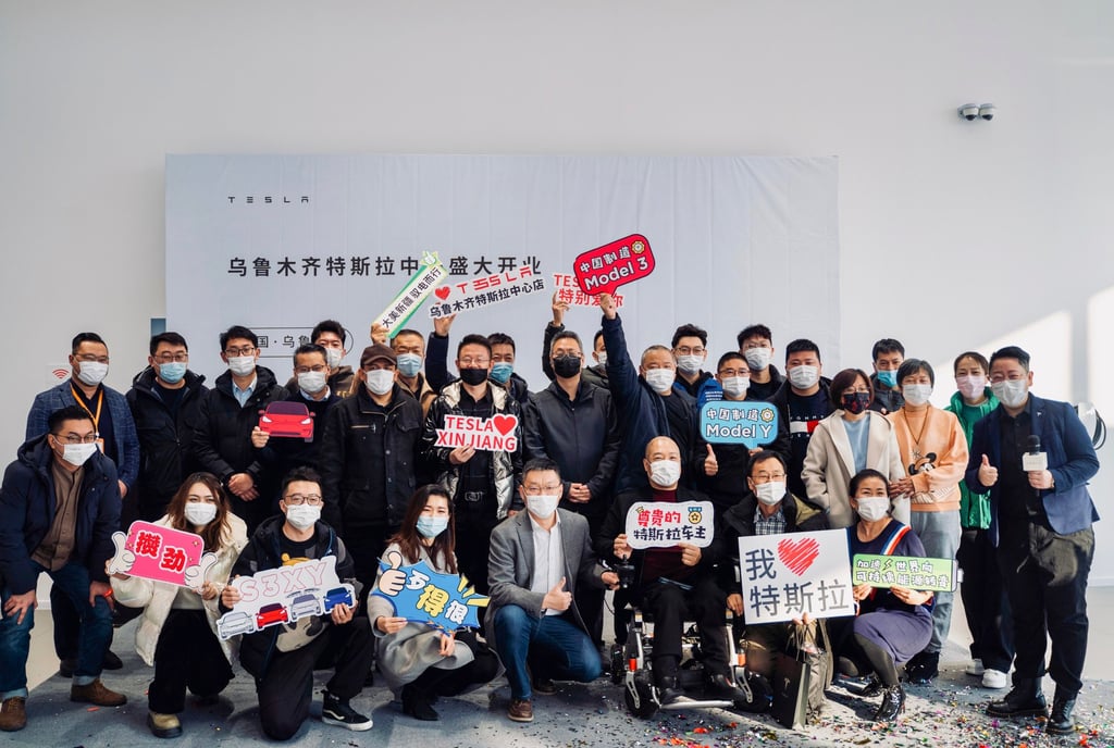 People hold signs including “Tesla [loves] Xinjiang” at the opening ceremony for the new showroom. Photo: Tesla/Weibo