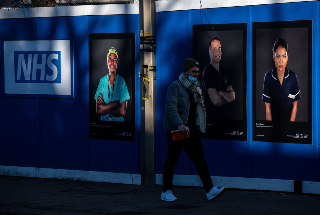 A pedestrian passes portraits of National Health Service (NHS) workers outside a temporary structure, to be used as a so-called Nightingale care hub, in the grounds of St. George’s Hospital in London on Friday. Photo: Bloomberg