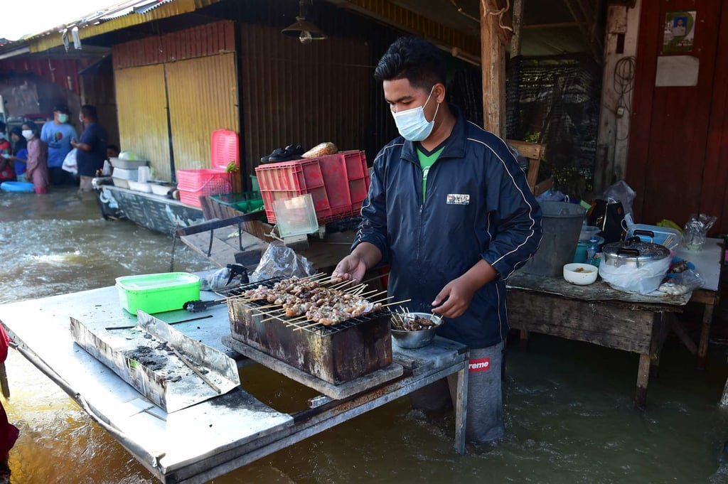 A man prepares roast chicken while standing in floodwaters following heavy rains in the southern Thai province of Narathiwat last month. Photo: AFP