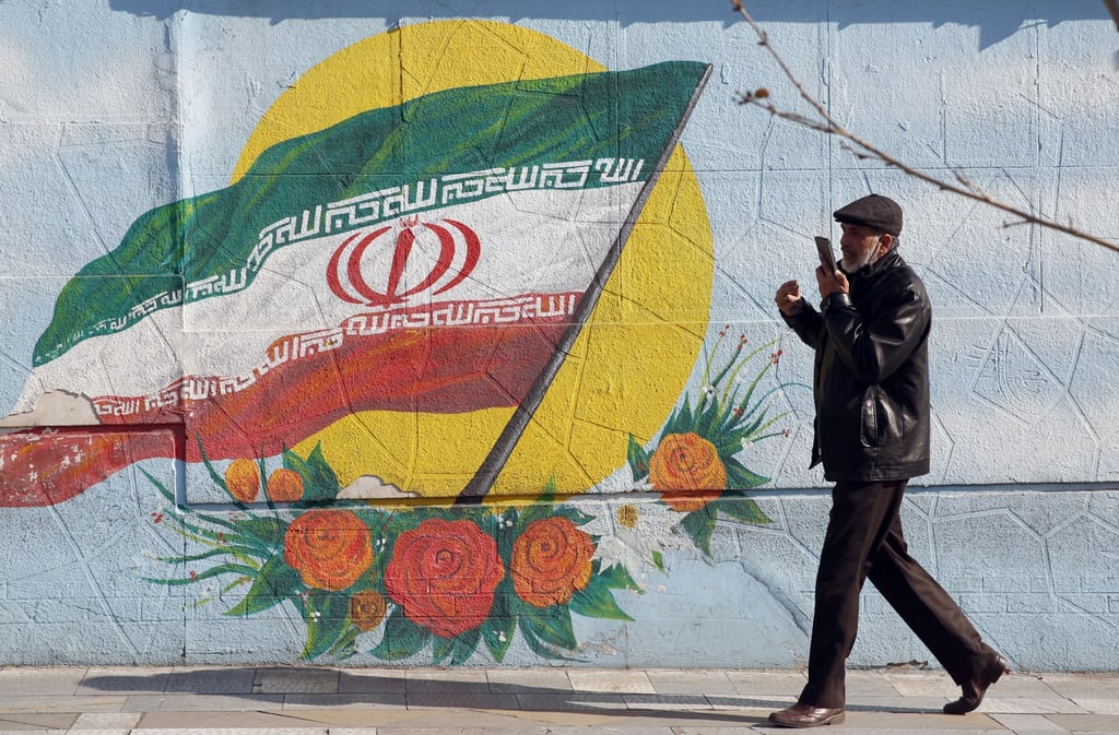 An Iranian man walks next to a wall painting of Iran’s national flag on a street in Tehran. Photo: EPA