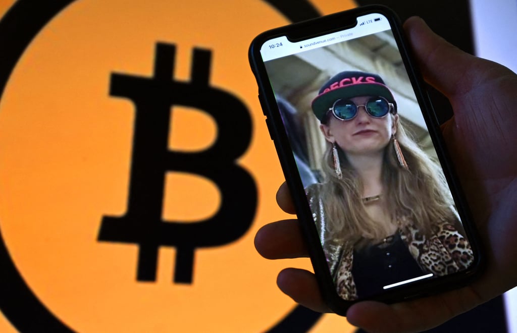 This illustration photo shows Heather Morgan, also known as “Razzlekhan,” on a phone in front of the bitcoin logo displayed on a screen, in Washington, DC, this month. She and her husband, Ilya Lichtenstein, have been charged with trying to launder some stolen Bitcoin. Photo: AFP