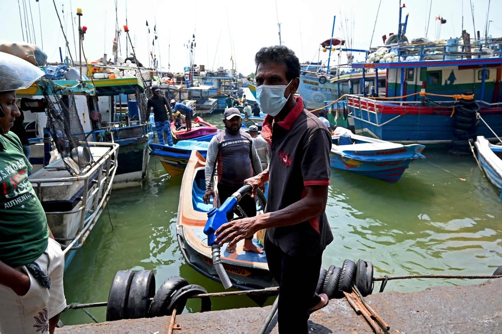 People stand over anchored fishing boats as they queue to buy kerosene oil in Negombo. Photo: AFP People stand over anchored fishing boats as they queue to buy kerosene oil in Negombo. Photo: AFP