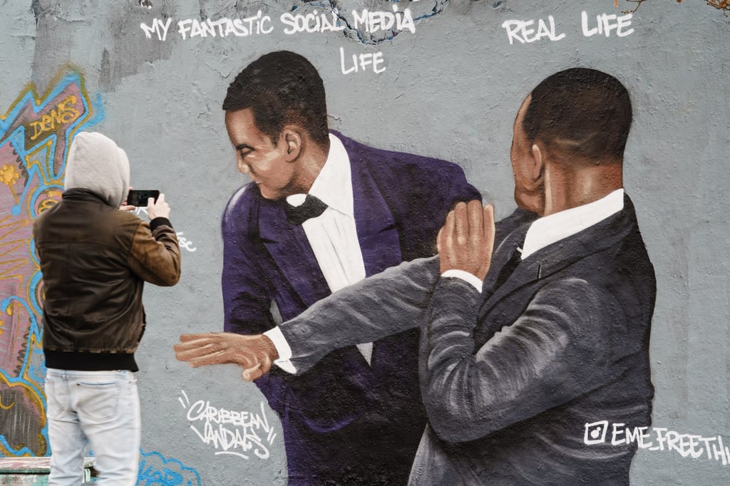 A passer-by takes a photo of a mural in Berlin artist Jesus Cruz Artiles, aka Eme Freethinker, depicting actor Will Smith slapping presenter Chris Rock in the face during the incident at the Oscars. Photo: EPA-EFE