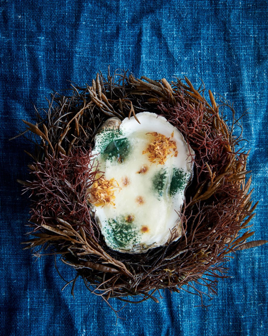 A dessert made with oyster stock, spirulina powder, roasted kelp, and fermented and smoked pumpkin, with quince and amazake ice cream, served in an oyster shell. Photo: Noma