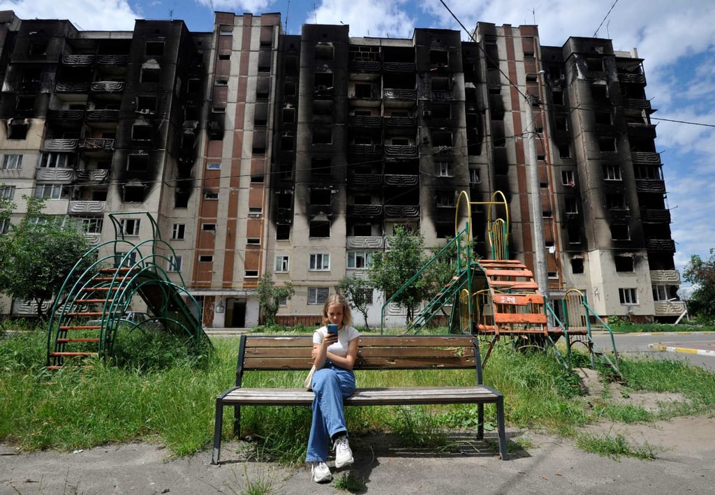 A girl looks at her smartphone in front of apartment buildings shelled in Irpin, near the Ukrainian capital of Kyiv, on Wednesday, as the Russian invasion entered its 113th day. Photo: AFP