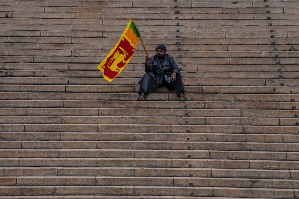 A protester sits holding the Sri Lankan flag outside the presidential secretariat in Colombo the day after Wickremesinghe was elected president. Photo: AP