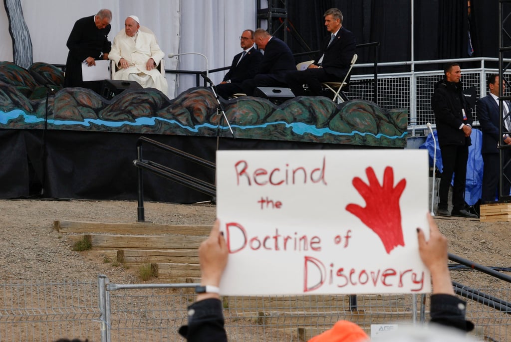 A person holds a protest sign as Pope Francis attends an event at Nakasuk School in Iqaluit, Canada on Friday. Photo: Reuters