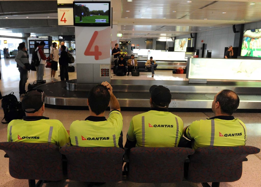 Qantas baggage handlers, seated, at Sydney International Airport. Photo: AFP Qantas baggage handlers, seated, at Sydney International Airport. Photo: AFP