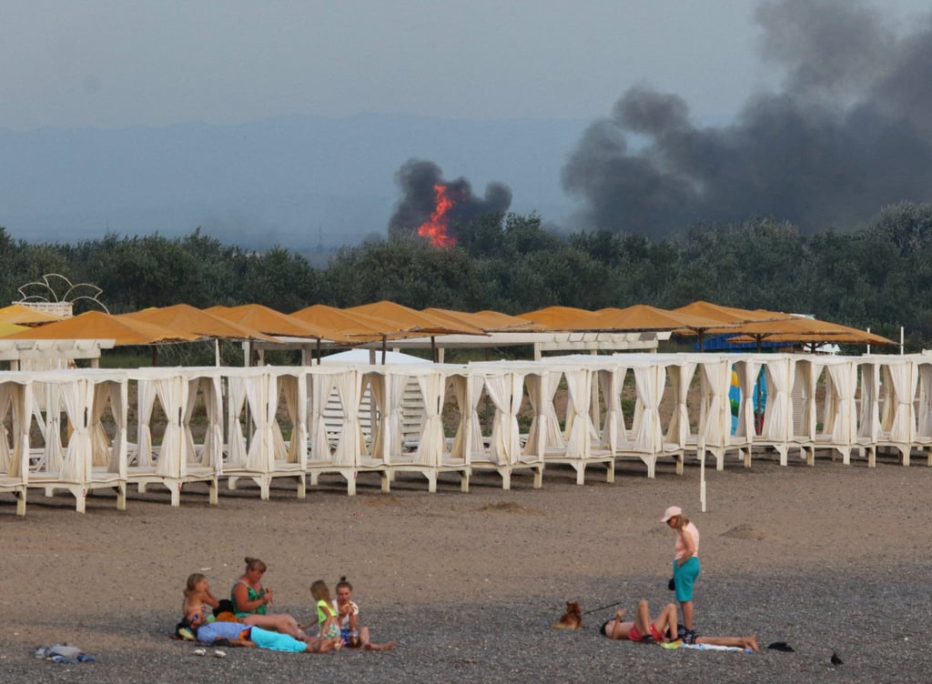 People rest on a beach as smoke and flames rise after explosions at a Russian military airbase in Novofedorivka, Crimea on Tuesday. Photo: Reuters