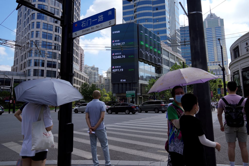 Pedestrians wait to cross a road junction near a display of stock indexes in Shanghai on August 3, 2022. A weak stock market and distressed property market are among the factors suppressing M&A activity. Photo: Reuters