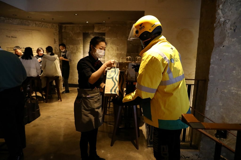 A staff member takes a bag of ordered food from a Meituan delivery worker during a media event of Starbucks launching a partnership with Meituan in Beijing on January 18, 2022. Photo: Reuters.