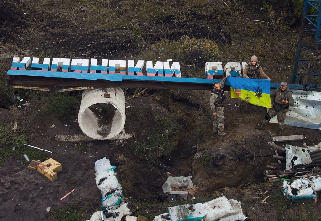 Ukrainian soldiers adjust the national flag on the damaged sign “Kupiansk district” close to recently retaken Kupiansk in the Kharkiv region. Photo: AP