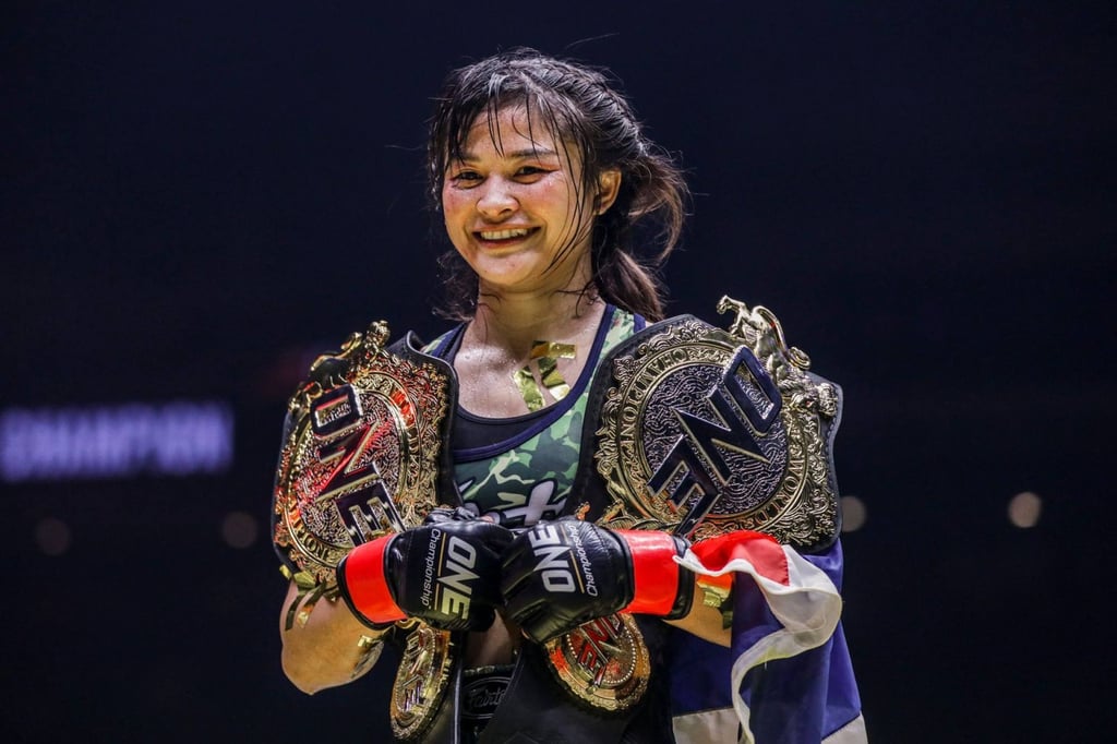 Stamp Fairtex holding the ONE atomweight Muay Thai and kickboxing belts. Stamp Fairtex holding the ONE atomweight Muay Thai and kickboxing belts.
