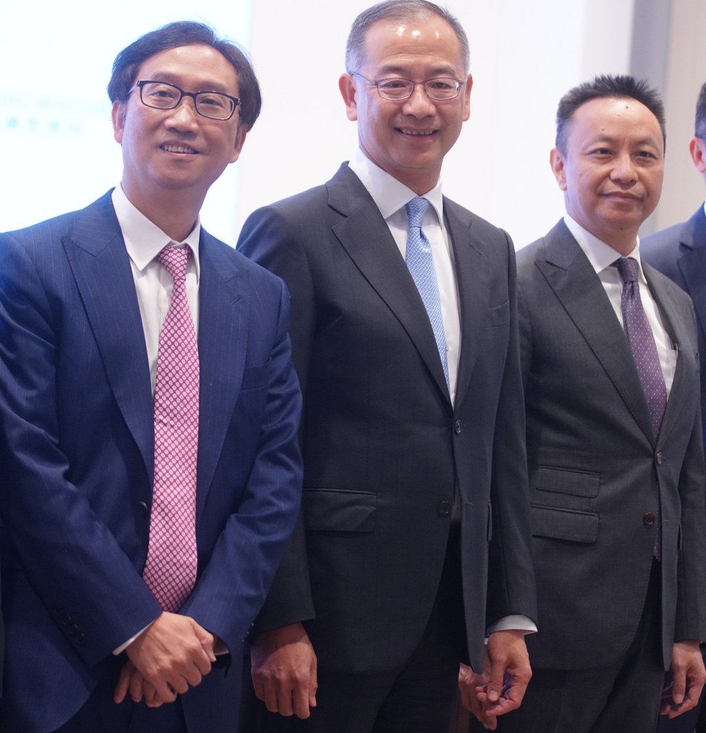 Three men in formal suits and ties are standing side by side at a professional event related to HKMA's stablecoin licensing and cryptocurrency regulation, smiling for the camera.