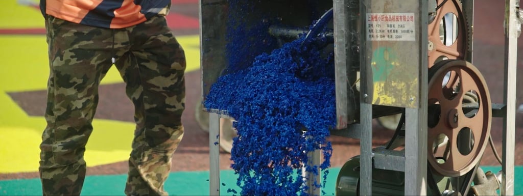 Bright blue raw materials made from upcycled old bicycle tyres are poured onto the ground to form the playing surface during construction of an outdoor sports area in rural China.