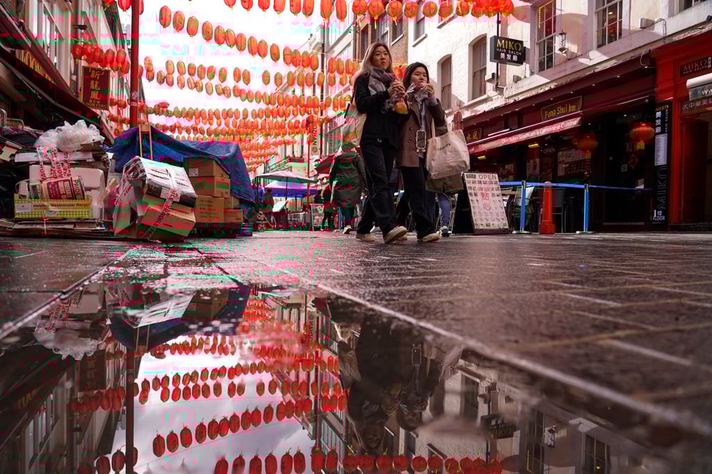 People are reflected in a puddle as they walk through Chinatown in London last month. Photo: AP