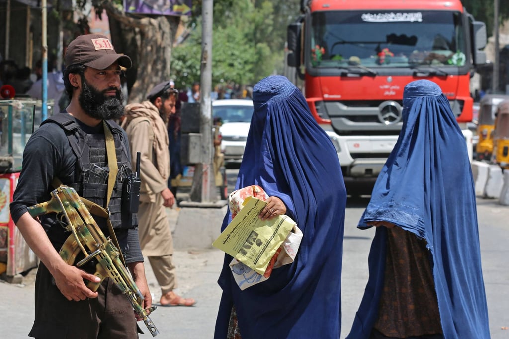 Afghan burqa-clad women walk past a Taliban security personnel along a street in Jalalabad. Photo: AFP