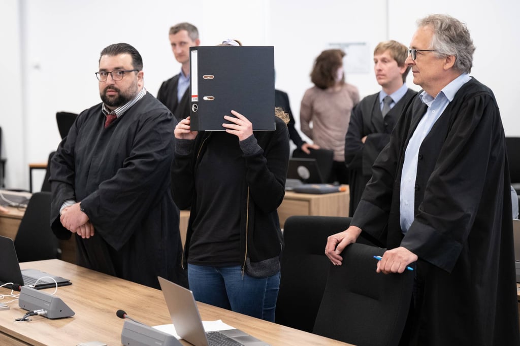 Defendant Lina E. holds a file folder in front of her face as she stands in the hearing room during the continuation of the trial at the Dresden Higher Regional Court. Photo: dpa