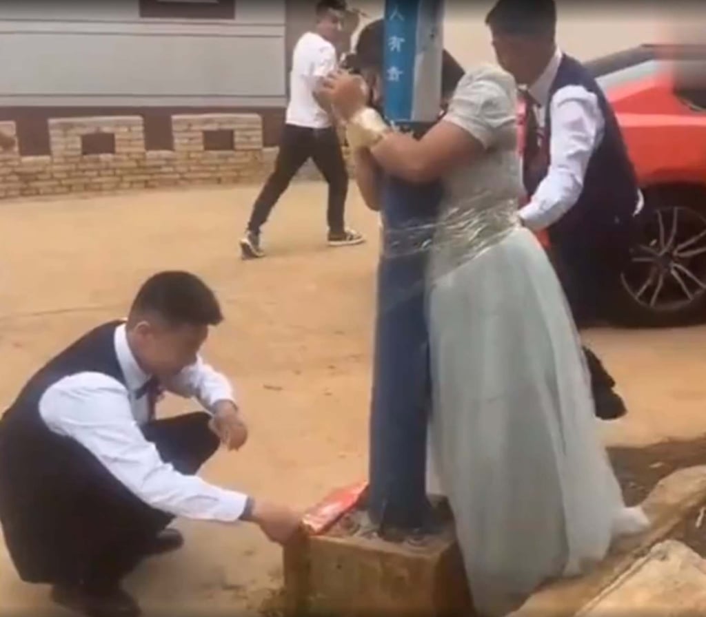 A bridesmaid is taped tight to a lamp post as a male member of the wedding party ignites firecrackers. Photo: Handout A bridesmaid is taped tight to a lamp post as a male member of the wedding party ignites firecrackers. Photo: Handout