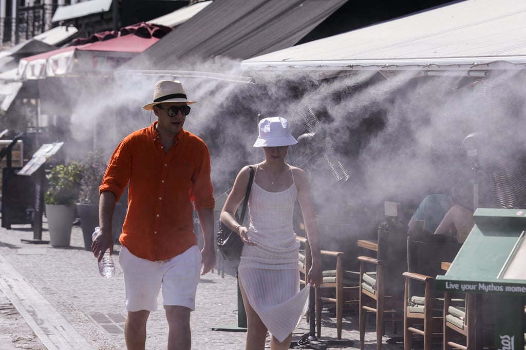 Tourists walk under a mist machine at a coffee shop to cool down in Athens, Greece on Sunday. Photo: Xinhua Tourists walk under a mist machine at a coffee shop to cool down in Athens, Greece on Sunday. Photo: Xinhua