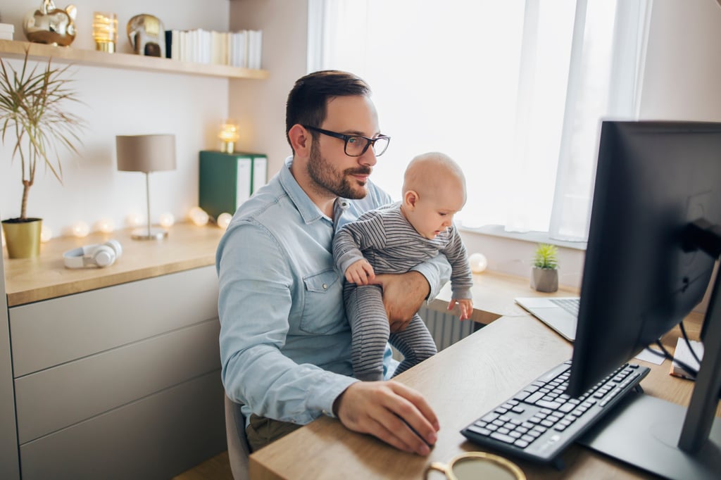 A man holds his son while working from home. The overwhelming desire for employers wanting workers back in the office seems largely tied to productivity monitoring. Photo: Shutterstock A man holds his son while working from home. The overwhelming desire for employers wanting workers back in the office seems largely tied to productivity monitoring. Photo: Shutterstock