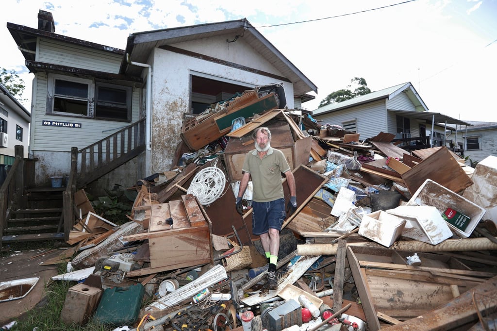 A man stands on a pile of his flood-damaged furniture outside his home in New South Wales last year. Flood-prone households have been the hardest hit by rising insurance premiums. Photo: AAP Image via AP