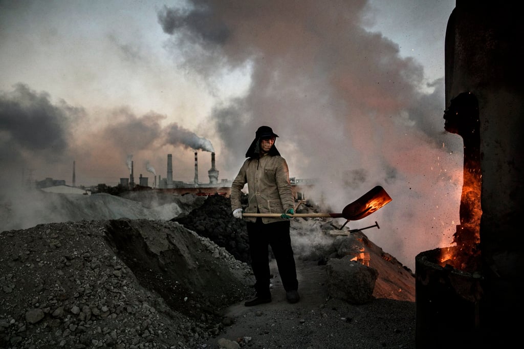 A Chinese labourer loads coal into a furnace as smoke and steam rises from an unauthorised steel factory in Inner Mongolia, China. Photo: Getty Images