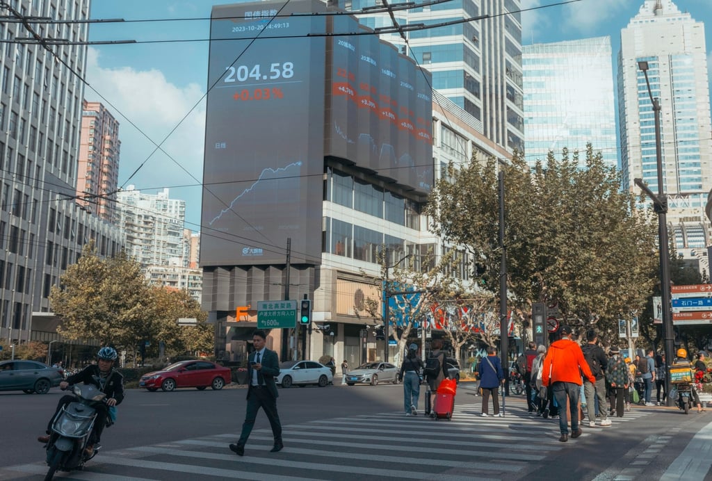 People cross on the street beneath a large screen showing the latest stock exchange and economy data, in Shanghai, China. Photo: EPA-EFE