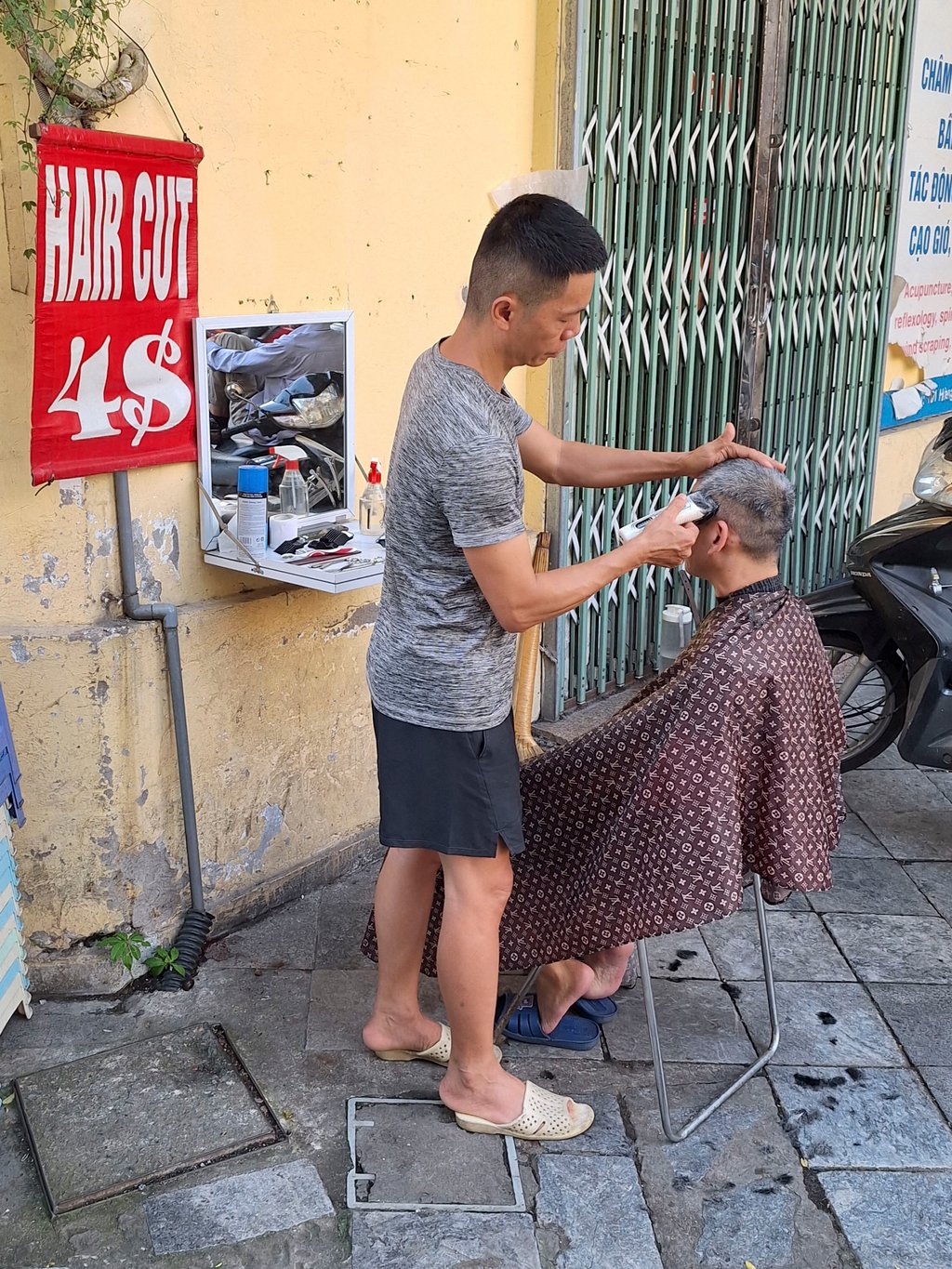A man receives a haircut on a street in Hanoi. Photo: Ed Peters