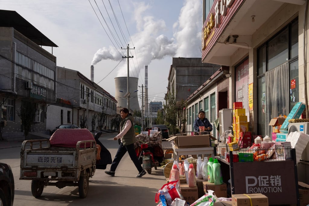 Guohua Power Station, a coal-fired power plant, operates as people sell items on a street in Dingzhou, Baoding, in northern China’s Hebei province. Photo: AP Guohua Power Station, a coal-fired power plant, operates as people sell items on a street in Dingzhou, Baoding, in northern China’s Hebei province. Photo: AP