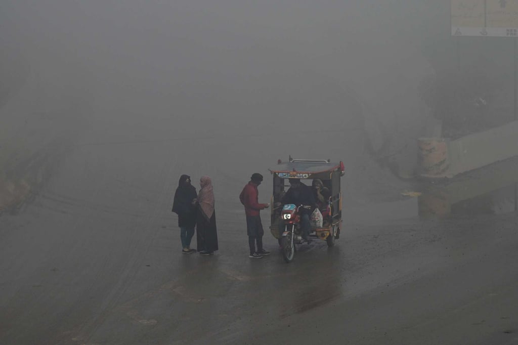 People stand by a road as another converses with a motorcycle-rickshaw driver amid heavy smog on the outskirts of Lahore earlier this week. PHOTO: AFP