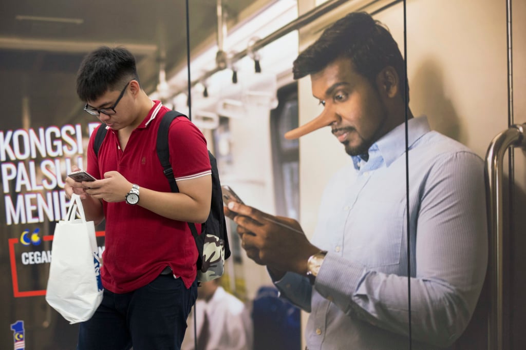 A commuter reads from his mobile phone next to an advertisement discouraging the dissemination of fake news at a railway station in Kuala Lumpur. Photo: AP A commuter reads from his mobile phone next to an advertisement discouraging the dissemination of fake news at a railway station in Kuala Lumpur. Photo: AP