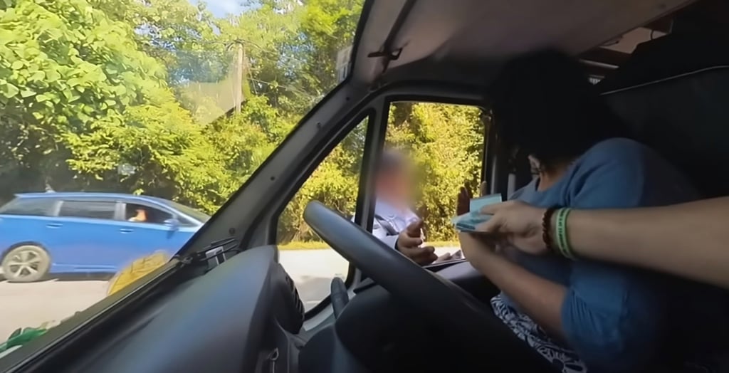 Chris Fisher hands cash to a policeman in Malaysia after being stopped for speeding in their Fiat Ducato van “Trudy” in this still from a social media video. Photo: YouTube/TreadTheGlobe Chris Fisher hands cash to a policeman in Malaysia after being stopped for speeding in their Fiat Ducato van “Trudy” in this still from a social media video. Photo: YouTube/TreadTheGlobe