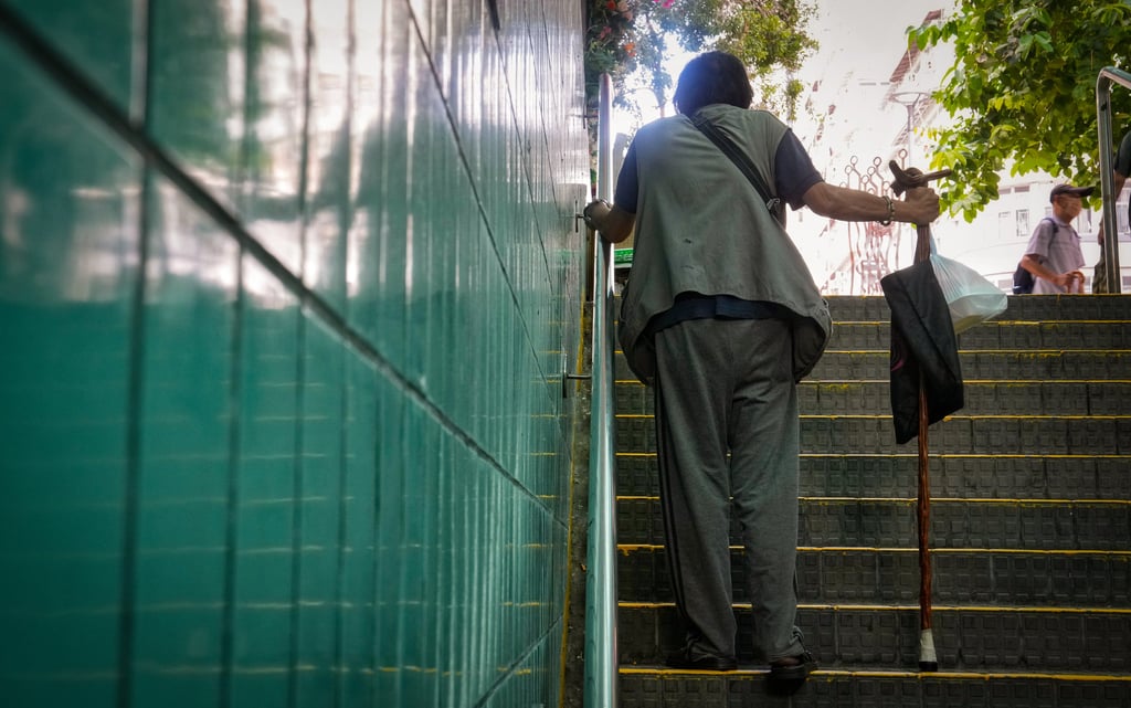 A man walks up the staircase to the exit of tunnel at Sham Shui Po with a crutch and a lunchbox. More than 188,000 people aged 65 and above live alone in Hong Kong. Photo: Elson Li
