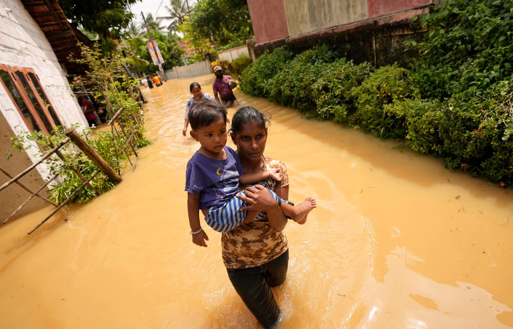A woman carries a child as she wades through a flooded street in Kochchikade, Sri Lanka, on November 10, 2021. Photo: AP