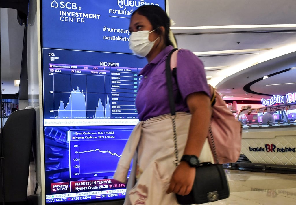 A woman wearing a face mask walks past an electronic board showing Asian stock index overview and news report on the oil market at a shopping centre in Bangkok. Photo: AFP